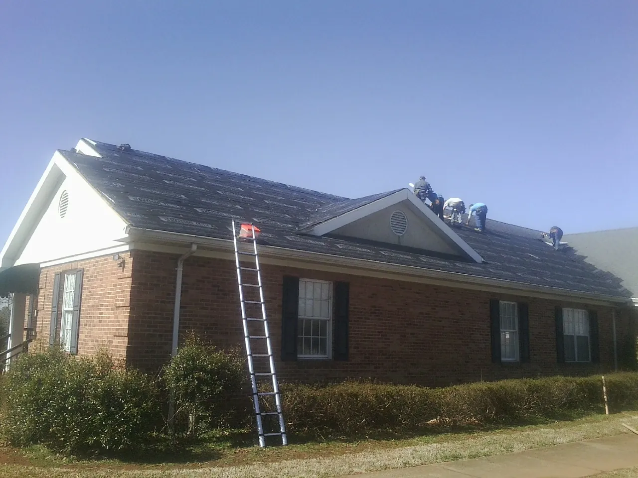 Crew tearing shingles off a brick ranch roof with a ladder set — Emergency Roof Repair work by our crew in Ceres