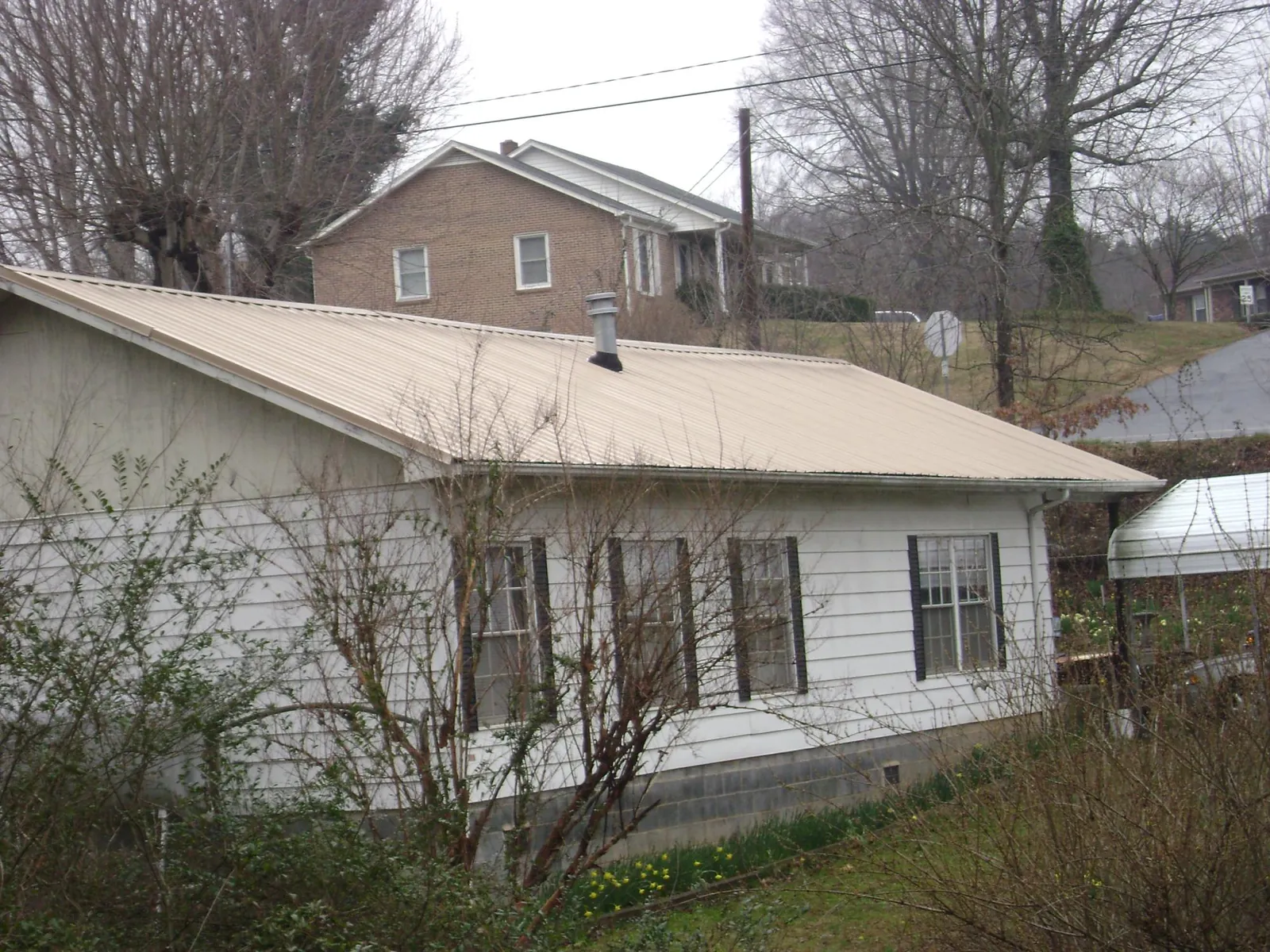 Tan metal roof on a white sided house set into a hillside — Commercial Roofing by Roofing Brothers in Ceres